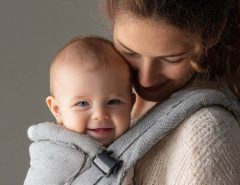 Parent wearing ergonomic baby carrier with happy newborn facing inward for bonding.