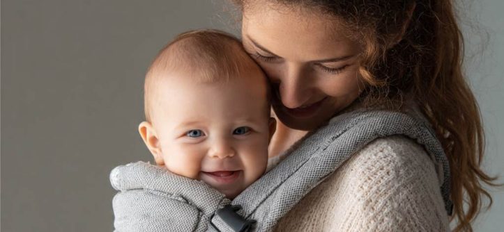 Parent wearing ergonomic baby carrier with happy newborn facing inward for bonding.