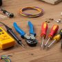 A beginner's DIY electrical kit laid out on a workbench, including a voltage tester, wire strippers, insulated screwdrivers, and electrical tape