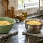 Side-by-side comparison of a plastic colander and a stainless steel pasta strainer on a kitchen countertop