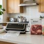 A compact vacuum sealer sitting on a kitchen counter next to sealed food bags.