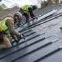 Roofing crew locking vertical metal panels together on a sloped roof