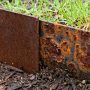 Metal garden edging showing weathered reddish brown Corten steel patina beside localized corrosion on untreated steel