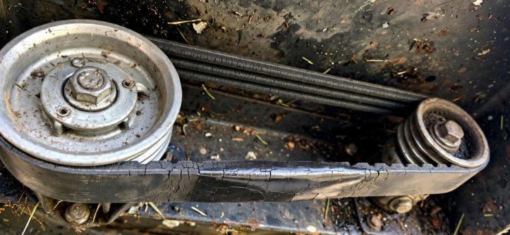 Self-propelled mower drive belt showing cracks and glazing beside pulleys