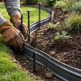 Landscaper installing flexible metal edging around a smooth curved flower bed, partially secured by ground stakes
