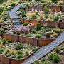 Sloping residential garden with stepped planting beds outlined by weathered steel edging